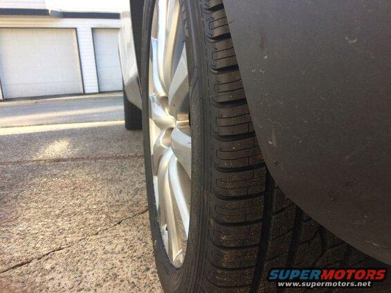 Side view of a car tire and silver alloy wheel, with a dark fender flare.