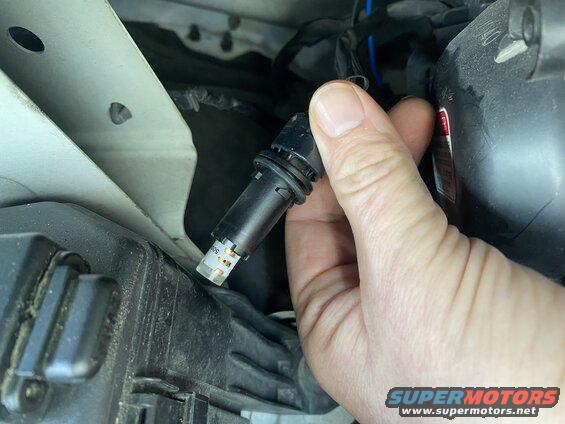 Hand holding a black automotive LED bulb near a black plastic component.