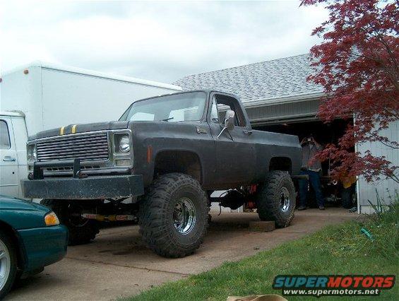Black lifted pickup truck with yellow hood stripes, chrome wheels, and large tires parked in a driveway