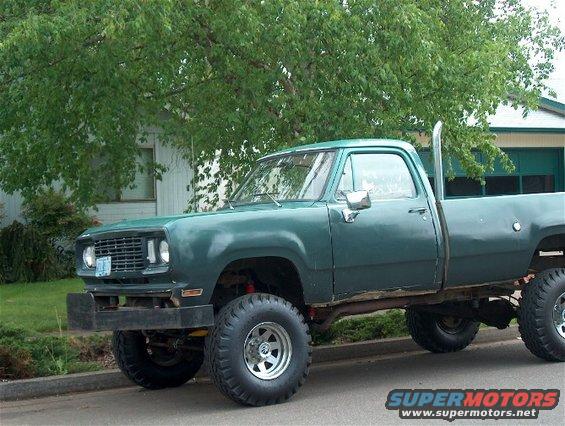 Green lifted pickup truck with large tires and side exhaust pipe parked in front of a house