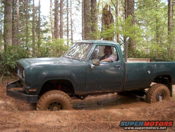 Green pickup truck stuck in mud with a man driving