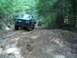 1979 Ford Bronco - Two trucks navigate a challenging muddy path through a dense forest.