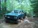 1979 Ford Bronco - A green pickup truck navigates a muddy trail in a wooded area, with another vehicle visible ahead.
