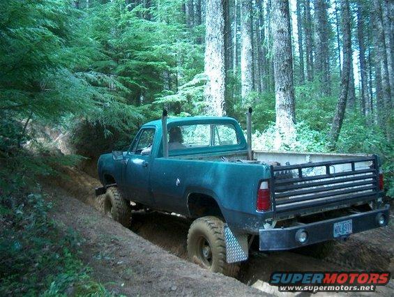 Teal pickup truck with side pipes driving on a muddy off-road trail