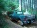 1979 Ford Bronco - This teal pickup truck navigates a challenging muddy off-road trail, its side pipes visible against the forest backdrop.