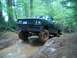 1979 Ford Bronco - Pickup truck navigates a muddy off-road trail in a wooded area.