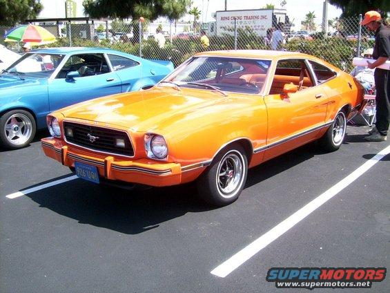Orange 1978 Ford Mustang II parked next to a blue car. License plate reads 9Z6 U91
