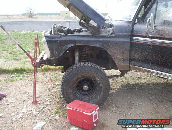 Front fender and wheel of a 1978 Ford Bronco with hood up, jacked up for work