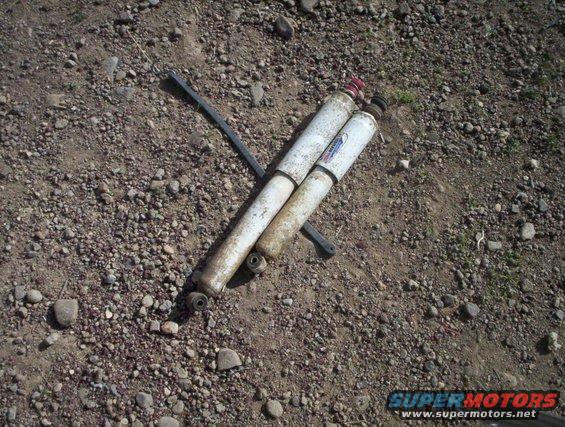 Two white shock absorbers with red and blue labels lying on gravel