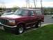 1994 Ford Bronco - A maroon Ford Bronco is parked outside on a cloudy day with other vehicles visible in the background.