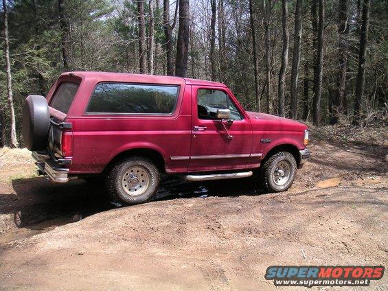 Red Ford Bronco with spare tire on rear, side view, on dirt road