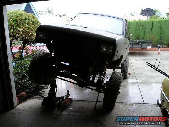 Front end of a lifted SUV, possibly a Bronco II, on jack stands in a garage. Modifications are visible