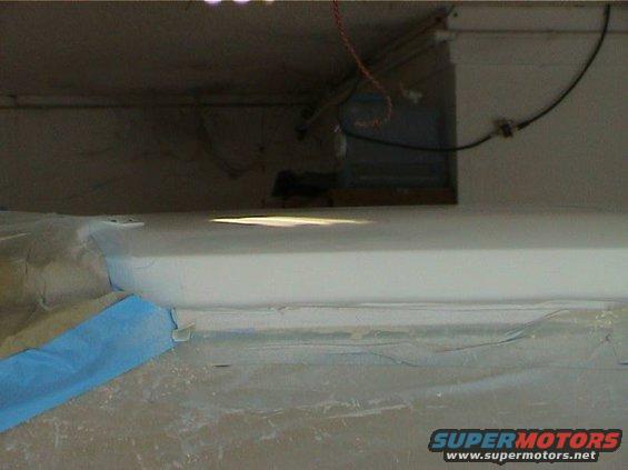 Close-up of a car's interior, possibly a dashboard or door panel, with blue tape and plastic sheeting. Supermotors.net logo visible
