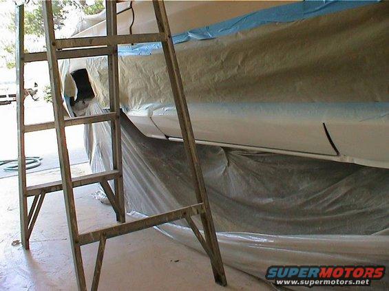 Ladder next to a white vehicle body covered in masking paper and plastic sheeting