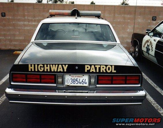 Rear view of a highway patrol car with 'HIGHWAY PATROL' on the trunk. Another patrol car is parked to the right
