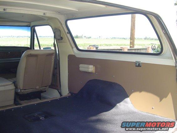 Interior shot of an older SUV, showing the rear cargo area and seats. View looks out the side window to a field