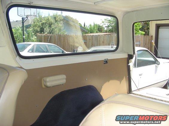 Interior of a 1979 Ford Bronco, showing tan door panel and beige seats, with a white car visible through the window