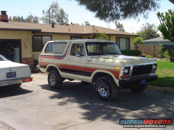 Cream-colored Ford Bronco with orange and brown side stripes parked next to a white car