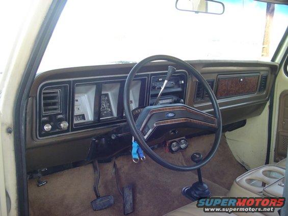 1979 Ford Bronco interior dashboard with wood grain trim, a Ford steering wheel, and brown carpet