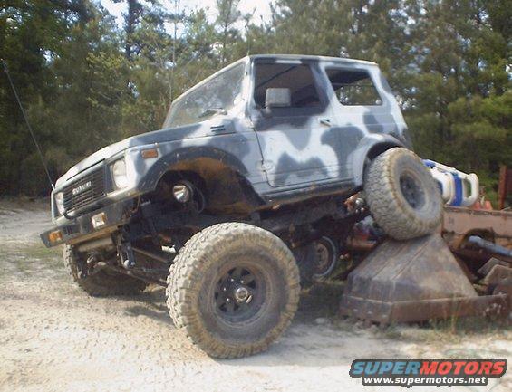 Suzuki Samurai with camouflage paint, lifted and on a dirt lot