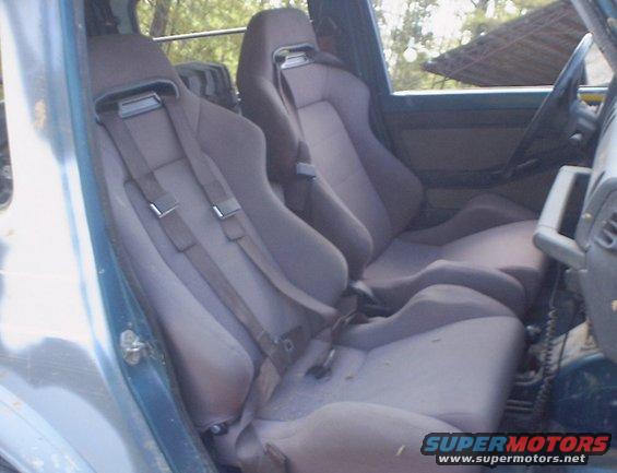 Interior view of a vehicle with two racing seats and five-point harnesses. A steering wheel is visible