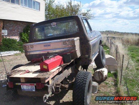 1978 Ford Bronco on a flatbed trailer, rear view, muddy condition, with a toolbox and red container on the bed