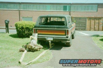 Rear view of a 1978 Ford Bronco with a tree stump being pulled by a strap attached to the hitch
