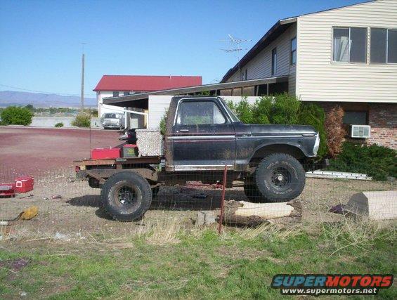 Black pickup truck with flatbed conversion, lifted, on logs, side view