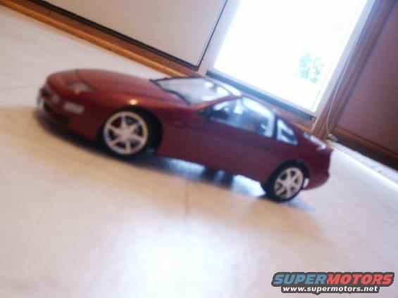 Red toy car on a light-colored floor, with a window in the background