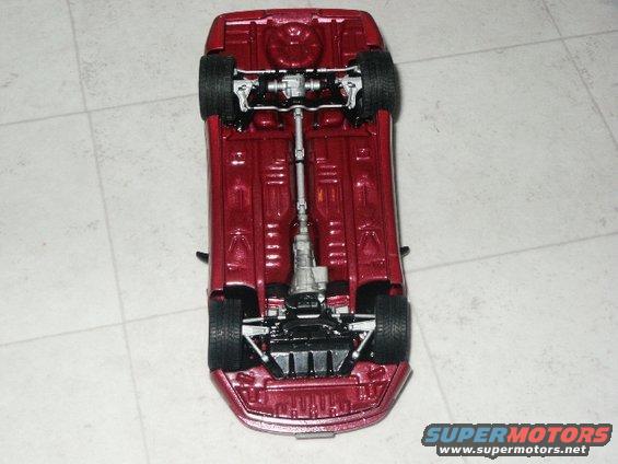 Underside view of a red model car showing the drivetrain and suspension components