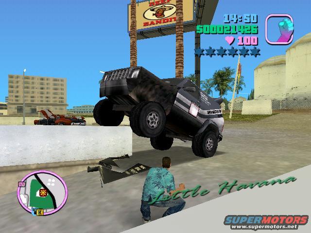Off-road truck with large tires, 3/4 front view. Another vehicle is visible in the background