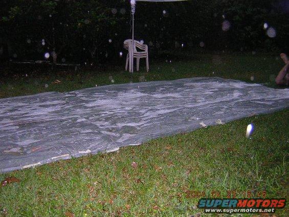 Tarp on grass with water droplets, chairs in background