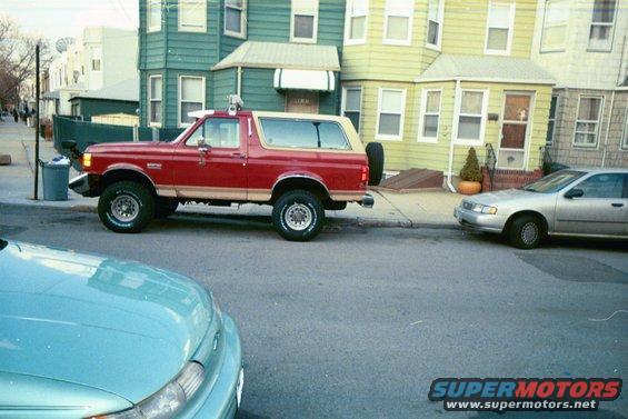 Red Ford Bronco parked on street, silver sedan next to it