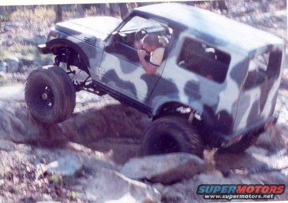 Suzuki Samurai with camouflage paint climbing over rocks on a trail
