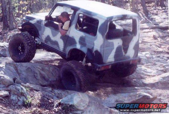Camouflaged Suzuki Samurai off-roading over rocks, driver visible