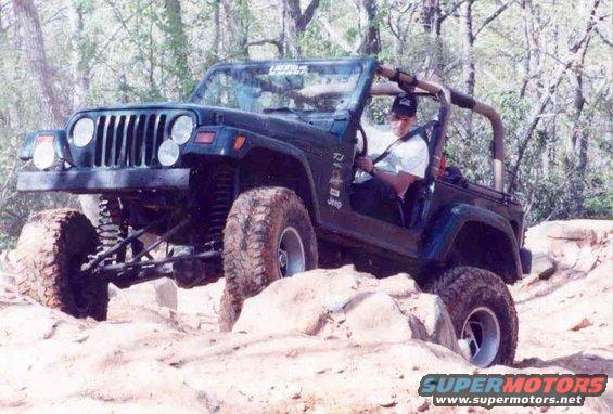 Dark green Jeep Wrangler climbing over rocks on a trail, driver visible