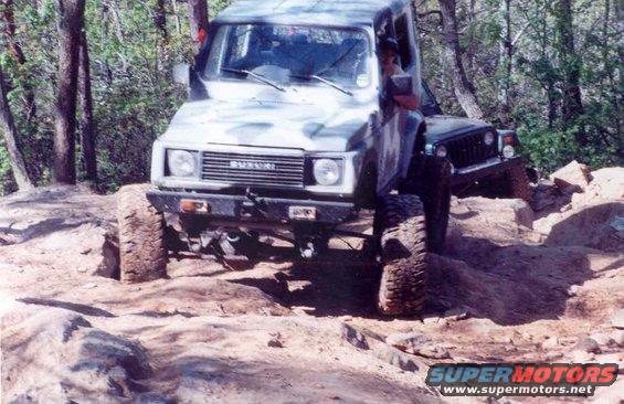 Suzuki Samurai on rocky terrain, front view, camouflage paint