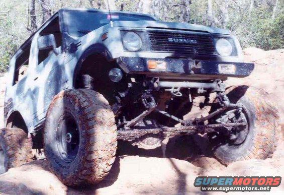 Suzuki Samurai with large tires on rocky terrain. The grille clearly shows 'SUZUKI'