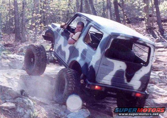 Camouflaged off-road vehicle climbing rocks, 3q-front view
