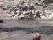 2000 Ford F-450 - Two trucks navigate a muddy terrain with a rocky cliff face in the background.