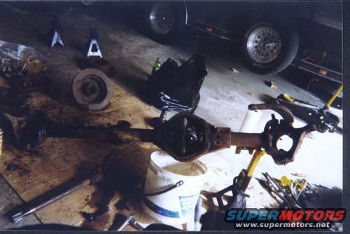 Differential and axle assembly on a wooden surface with tools and a white bucket