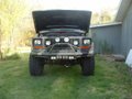 Front view of a lifted Jeep Cherokee XJ with aftermarket bumper and lights, hood up