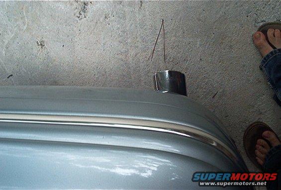 Close-up of a chrome antenna base on a silver car bumper with a chrome trim strip. Two thin wires stick out of the antenna base. Feet in sandals are visible on the right