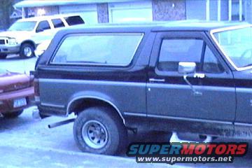 Side view of a two-tone 1987 Ford Bronco parked next to a red car and a white SUV