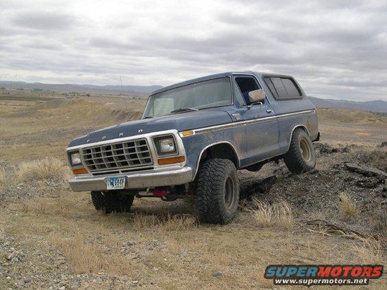 Blue 1978 Ford Bronco with lifted suspension driving off-road