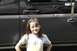 1989 Ford Bronco - A young girl stands in front of a dark-colored SUV.