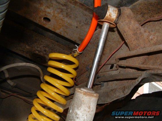 Close-up of a yellow coil spring and shock absorber assembly with an orange hose