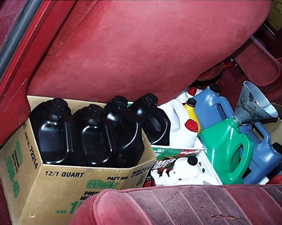 Red velour seats in a vehicle interior filled with various oil containers and a funnel