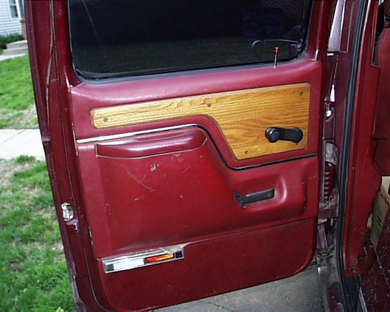 Maroon car door panel with wood trim, black handle, and chrome accent