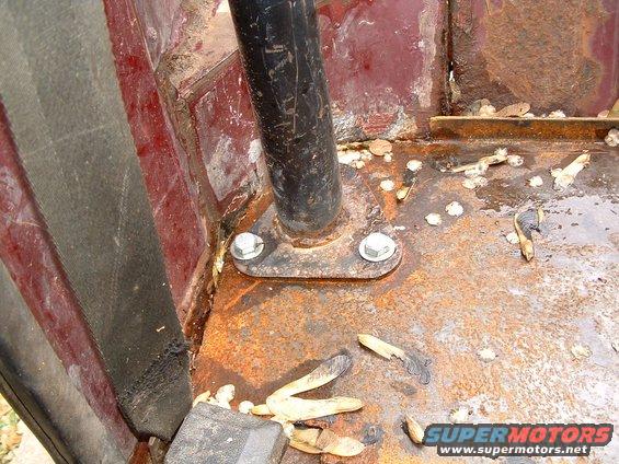 Interior floor of a vehicle with a rusted roll bar mount and seatbelt